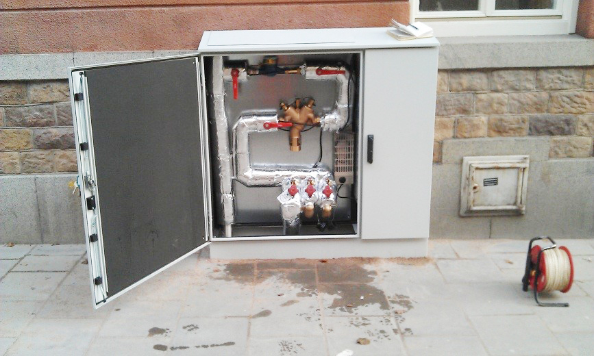 Ett öppet skåp längs en trottoar. Inne i skåpet syns rör och regleringskranar.