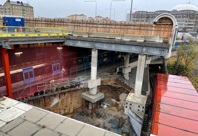 Bredvid ett tunnelbanetåg i rullning ligger ett arbetsområde. I bakgrunden syns Globen.