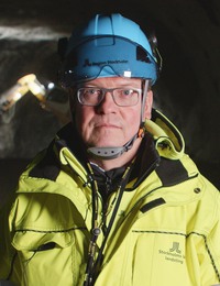 Man i gul varseljacka och bygghjälm står i en tunnel.