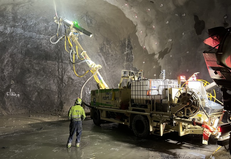 En stor maskin står framför en bergvägg och sprutar betong.