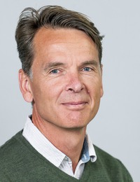 Bild på en man med vit skjorta och grön tröja.