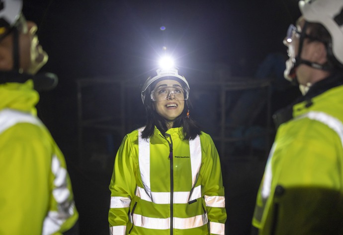 Tre personer i gul väst titta upp i taket i mörk tunnelmiljö.