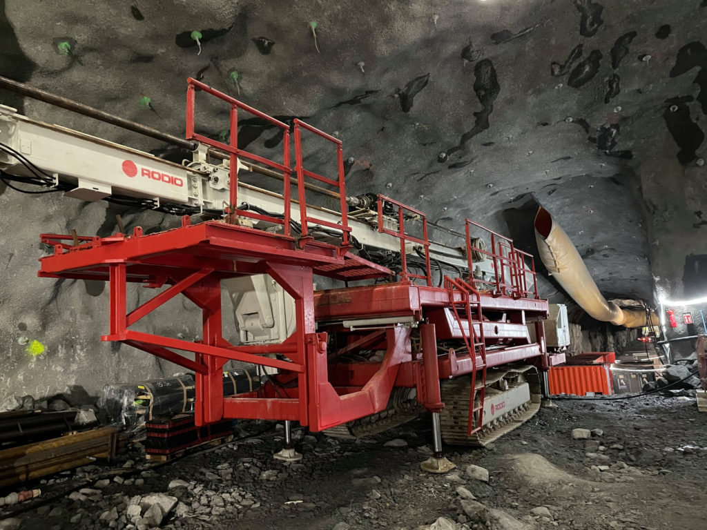 En stor röd maskin på bandvagn står inne i en tunnel.