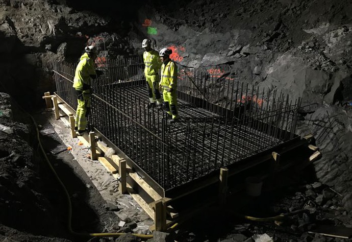 Tre personer står på en fyrkantig konstruktion av armeringsjärn i en mörk tunnel.