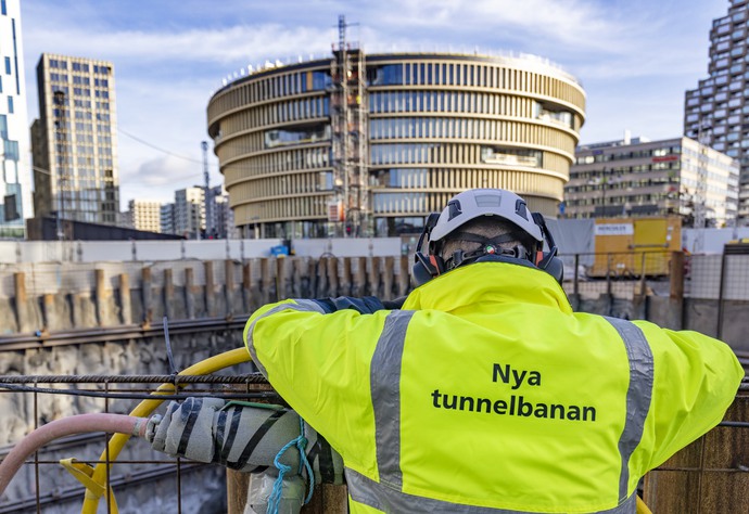 Man i gul arbetsjacka med texten Nya tunnelbanan på ryggen tittar ut över ett arbetsområde i Hagastaden.