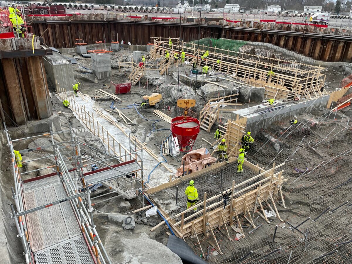 Arbetsområde med bland annat pågående betongarbeten. Byggnadsarbetare arbetar på flera ställen.